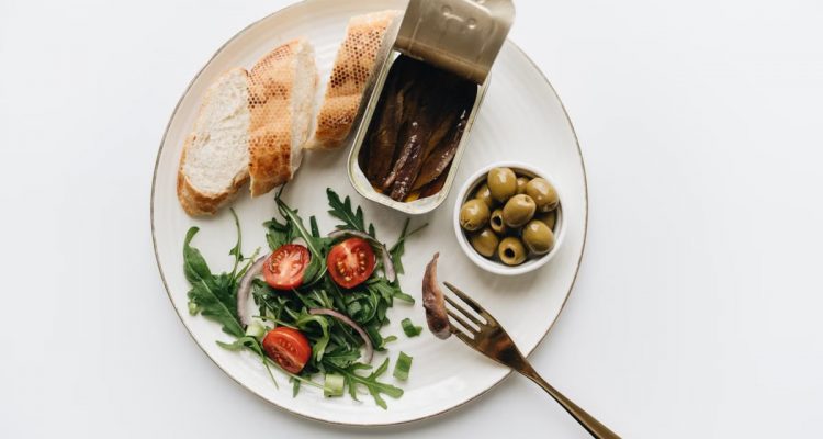A gourmet Mediterranean dish featuring anchovies, olives, bread, and fresh salad on a plate.
